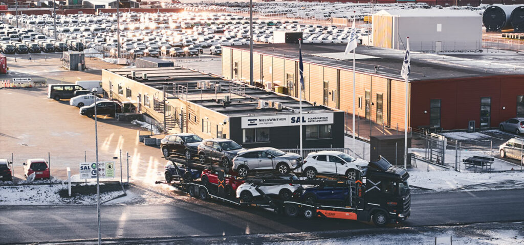 Auto transport truck exiting SAL's Auto terminal. In the background, numerous cars are seen at the Terminal.